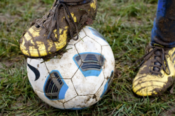 Close up of a muddy football shoe standing on muddy football on a muddy field.