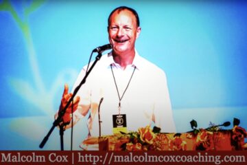 Malcolm Cox standing at a podium giving a talk.